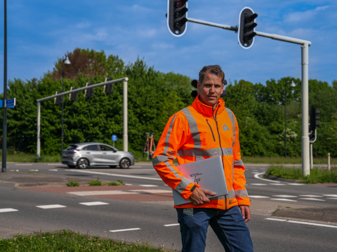 Medewerker van ViaMobility staat op een kruispunt met laptop in zijn arm